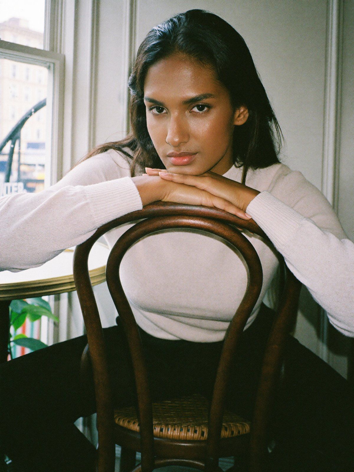 Café chair, backwards: a woman rests her arms on a chair back, a window behind her