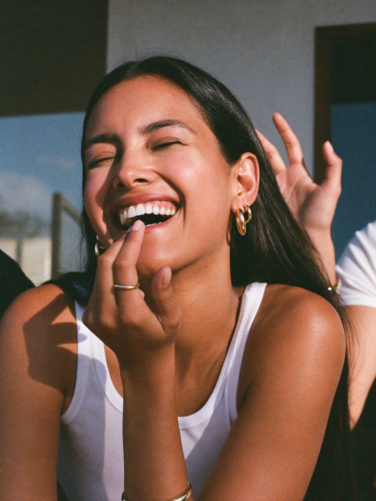 Laugh, close: a woman laughs with her eyes shut and a hand at her mouth
