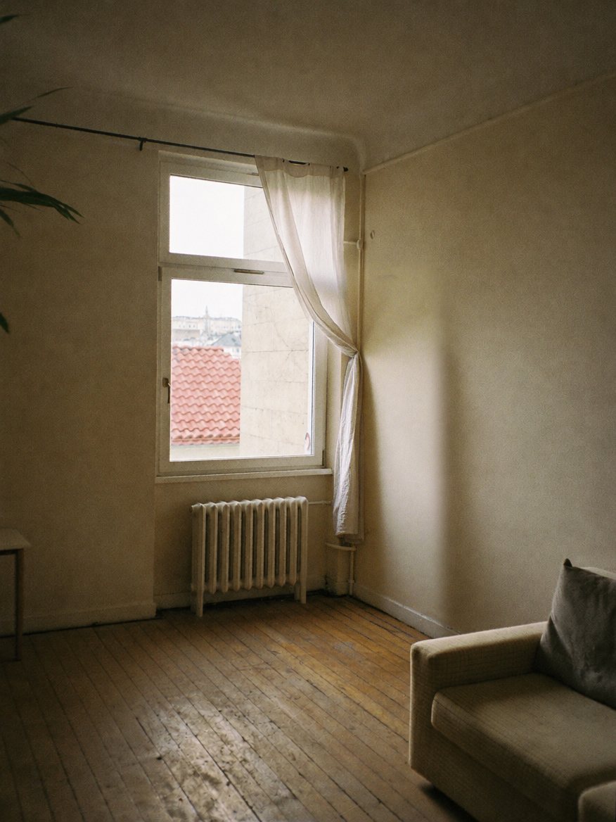 An ordinary living room with a tall window, a radiator and a sofa